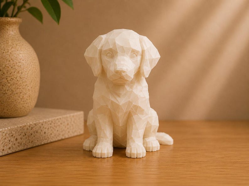 May include: A cream-colored, geometric-style dog figurine featuring a faceted, low-poly design. The sculpture depicts a puppy in a seated position with floppy ears, a smooth surface, and sharp, angular edges forming its body and facial features.
