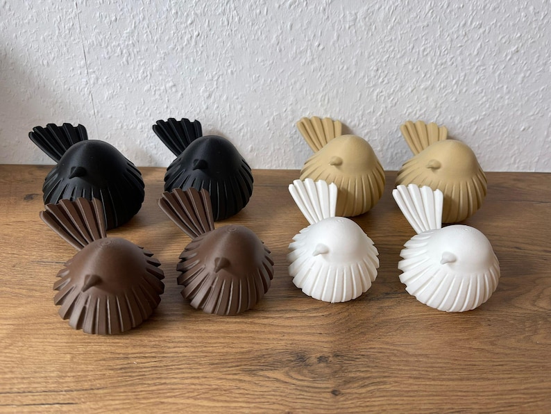 May include: Eight small bird figurines arranged in pairs, featuring two black, two brown, two tan, and two white birds. Each bird has a rounded body with vertical ribbed detailing and a fanned tail, all crafted with a smooth, matte finish.