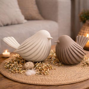 May include: Two bird figurines with a smooth, rounded body and a ribbed, fanned tail design. One bird is off-white and the other is a muted taupe brown. Both figures feature a pointed beak and a minimalist, solid construction with a matte finish.