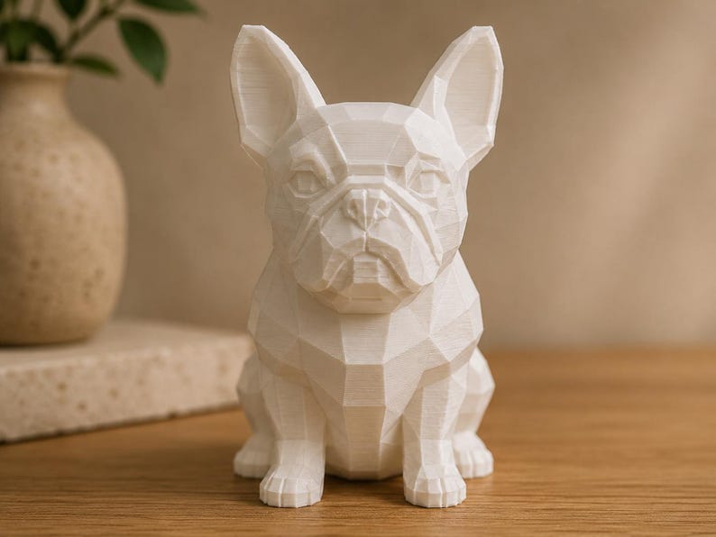 May include: A white, low-poly geometric sculpture of a French Bulldog. The figure features sharp, angular facets that define the dog's ears, snout, and body shape, creating a structured, multi-faceted appearance with a matte finish.