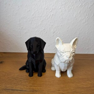 May include: Two geometric dog figurines, one black and one white, featuring a faceted, low-poly design. The black figurine resembles a Labrador Retriever, while the white figurine resembles a French Bulldog, both sitting in an upright, alert posture.