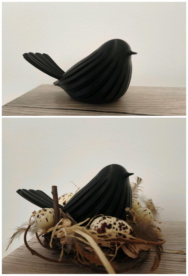 May include: A matte black bird figurine with a ribbed texture on its body and a pointed beak. The second view shows the same black bird figurine nestled inside a small bird's nest filled with speckled cream-colored eggs and brown feathers.