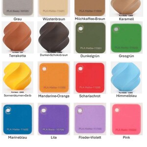 May include: A collection of twenty-three PLA filament color swatches, including square and twisted shapes. Each swatch features a hole for hanging and is labeled with its specific color name and product code, such as Kohlschwarz, Nardo-Grau, and Karamell.