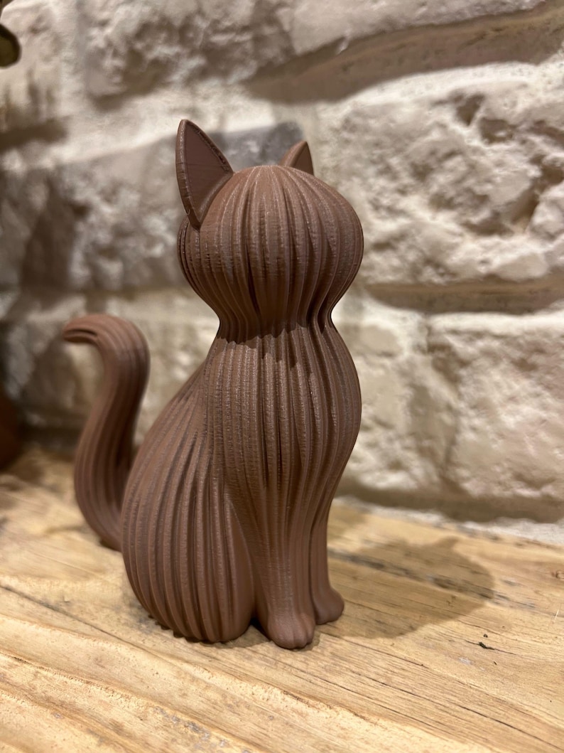 May include: A brown cat figurine featuring a distinct ribbed or layered texture across its entire body. The cat is depicted in a seated position with its tail curved upward, showcasing a vertical linear pattern that defines its form.