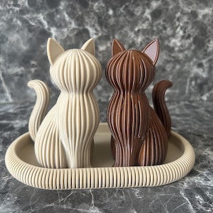 Zwei moderne Katzen-Skulpturen aus nachhaltigem PLA im minimalistischen Design. Das Duo in Wüstenbraun und Dunkel-Schokobraun zeigt die feine gerippte Textur des 3D-Drucks und ist auf einer farblich abgestimmten Schale arrangiert. Ideal als skandinavische Tischdeko.
Die Schale ist nicht im Bestellumfang enthalten.