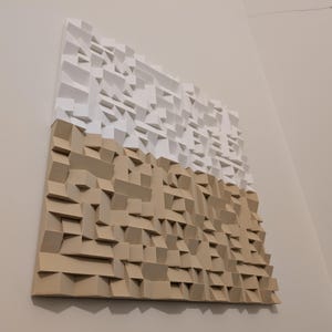 May include: A square wall-mounted acoustic panel featuring a three-dimensional geometric design. The top half is composed of white blocks, while the bottom half consists of tan blocks, creating a textured surface with varying depths.