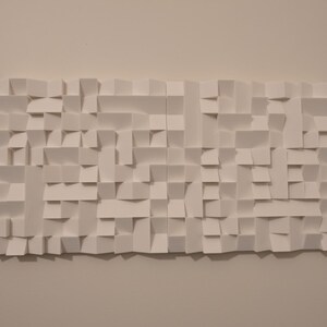 May include: A rectangular white wall art piece composed of numerous folded paper segments creating a three-dimensional geometric relief pattern with varying depths and shadows across the entire surface of the structure.