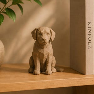 May include: A light brown, geometric-style dog figurine with a faceted, angular surface texture. The sculpture depicts a seated dog with floppy ears, a defined snout, and a neutral expression, crafted with a matte finish and solid construction.