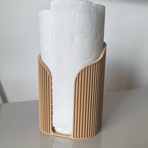 May include: A light tan, vertically ribbed paper towel holder with a U-shaped front cutout, containing a roll of white paper towels with a circular embossed pattern on the surface of the paper.