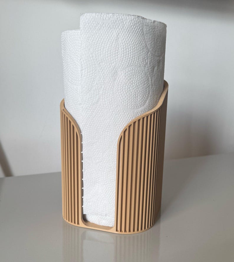 May include: A light tan, vertically ribbed paper towel holder with a U-shaped front cutout, containing a roll of white paper towels with a circular embossed pattern on the surface of the paper.