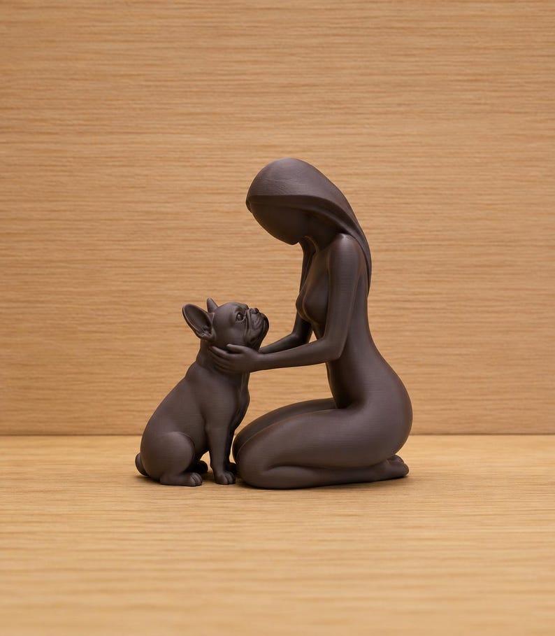 May include: A dark brown matte figurine depicting a kneeling person with long hair gently cupping the face of a French Bulldog. The sculpture features smooth, minimalist curves and a solid, monochromatic finish, capturing a quiet interaction.