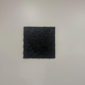 May include: A square wall art piece composed of numerous small, black, rectangular blocks of varying heights and depths, creating a textured, three-dimensional grid pattern across the entire surface of the object.