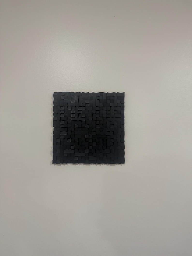 May include: A square wall art piece composed of numerous small, black, rectangular blocks of varying heights and depths, creating a textured, three-dimensional grid pattern across the entire surface of the object.