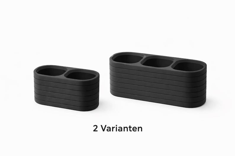 May include: Two matte black organizers with rounded rectangular shapes. The smaller organizer features two circular compartments, while the larger one has three. Both items display horizontal ribbed detailing and the text 2 Varianten.