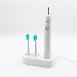 以下が含まれることがあります： 2つの交換用ブラシヘッドと充電ベースを備えた白い電動歯ブラシ。ブラシヘッドはターコイズ色の毛です。歯ブラシのハンドルには緑色の電源ボタンと「sonicare」のブランド名があります。白いコードがベースから伸びています。