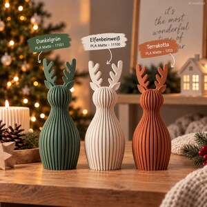 May include: Three reindeer figurines with vertical ribbed textures, colored dark green, off-white, and terracotta. Each features antlers and a rounded body. Labels indicate Dunkelgr&uuml;n 11501, Elfenbeinwei&szlig; 11100, and Terrakotta 1203, all PLA Matte.