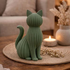 May include: A sage green cat figurine featuring a vertical ribbed texture across its entire body. The cat is depicted in a seated position with its tail curled upward, showcasing a smooth matte finish and a stylized, geometric form.