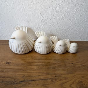May include: A set of four off-white bird figurines arranged in a row from largest to smallest. Each bird features a smooth, rounded body with vertical carved lines along the sides and a fanned-out tail. The birds have small, pointed beaks.