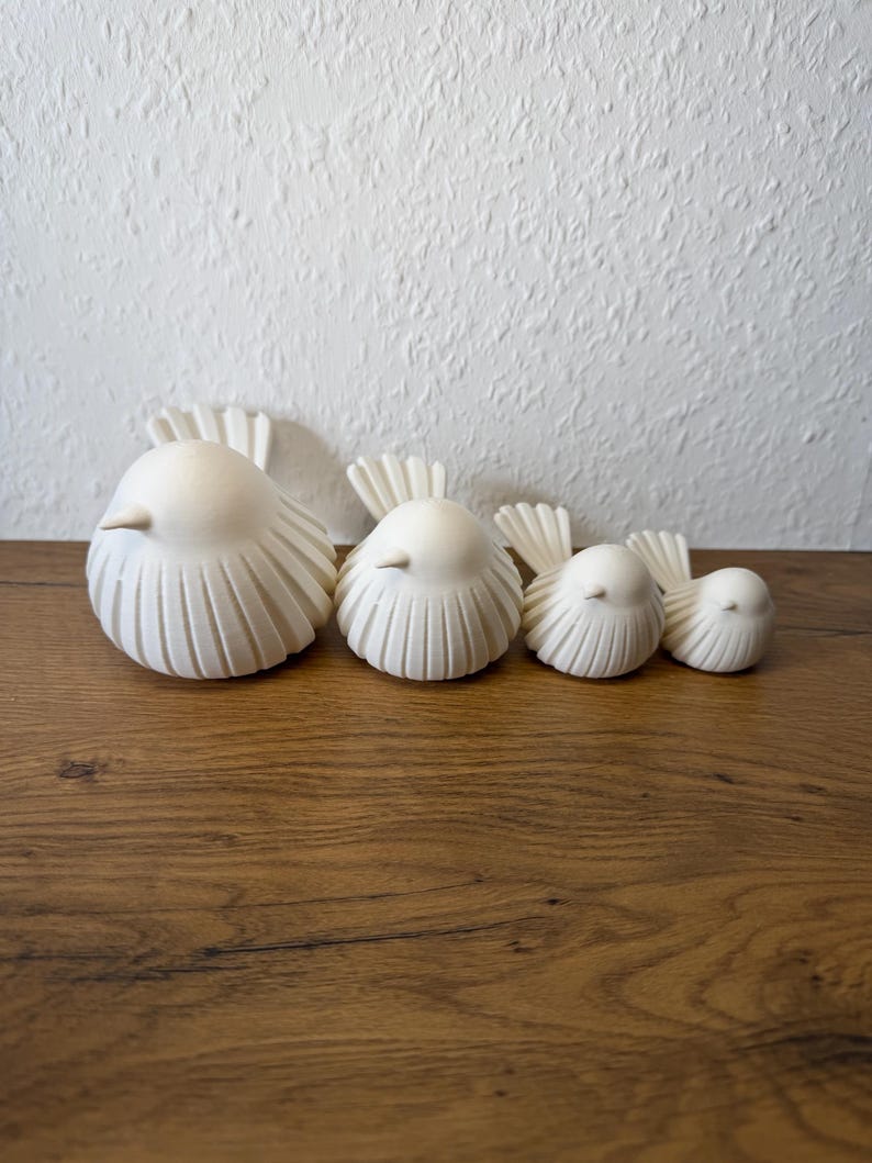 May include: A set of four off-white bird figurines arranged in a row from largest to smallest. Each bird features a smooth, rounded body with vertical carved lines along the sides and a fanned-out tail. The birds have small, pointed beaks.