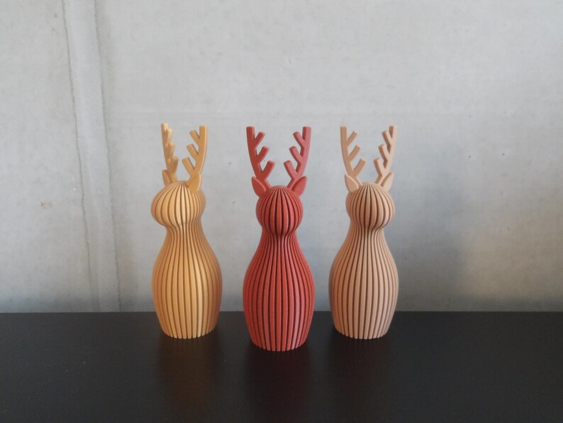 May include: Three standing reindeer figurines featuring a vertical ribbed texture. The left figure is yellow, the center figure is dark red, and the right figure is light tan. Each reindeer has a rounded body and branched antlers.