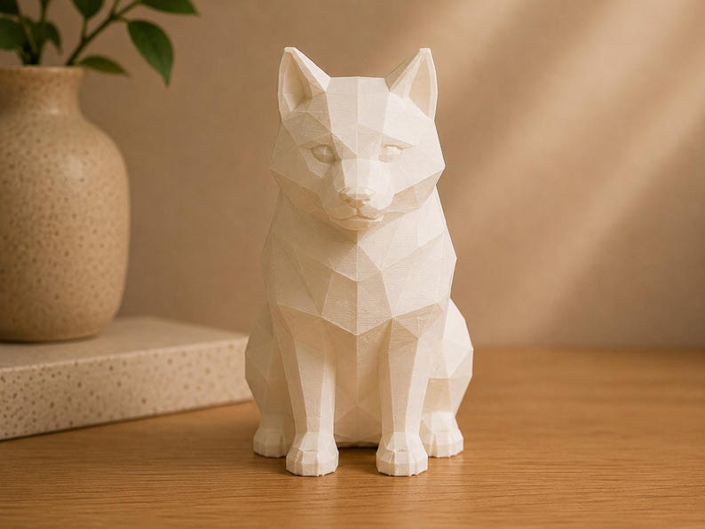 May include: A white, low-poly geometric sculpture of a sitting dog. The figure features sharp, angular facets that define the canine's ears, snout, and body structure, creating a clean, faceted appearance throughout the entire form.