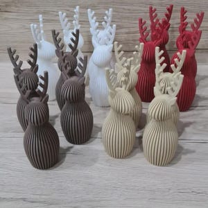 May include: A collection of twelve small, three-dimensional reindeer figurines arranged in rows. The figures are crafted with a ribbed, vertical texture and feature prominent antlers. They are available in four distinct colors: white, dark brown, beige, and red.