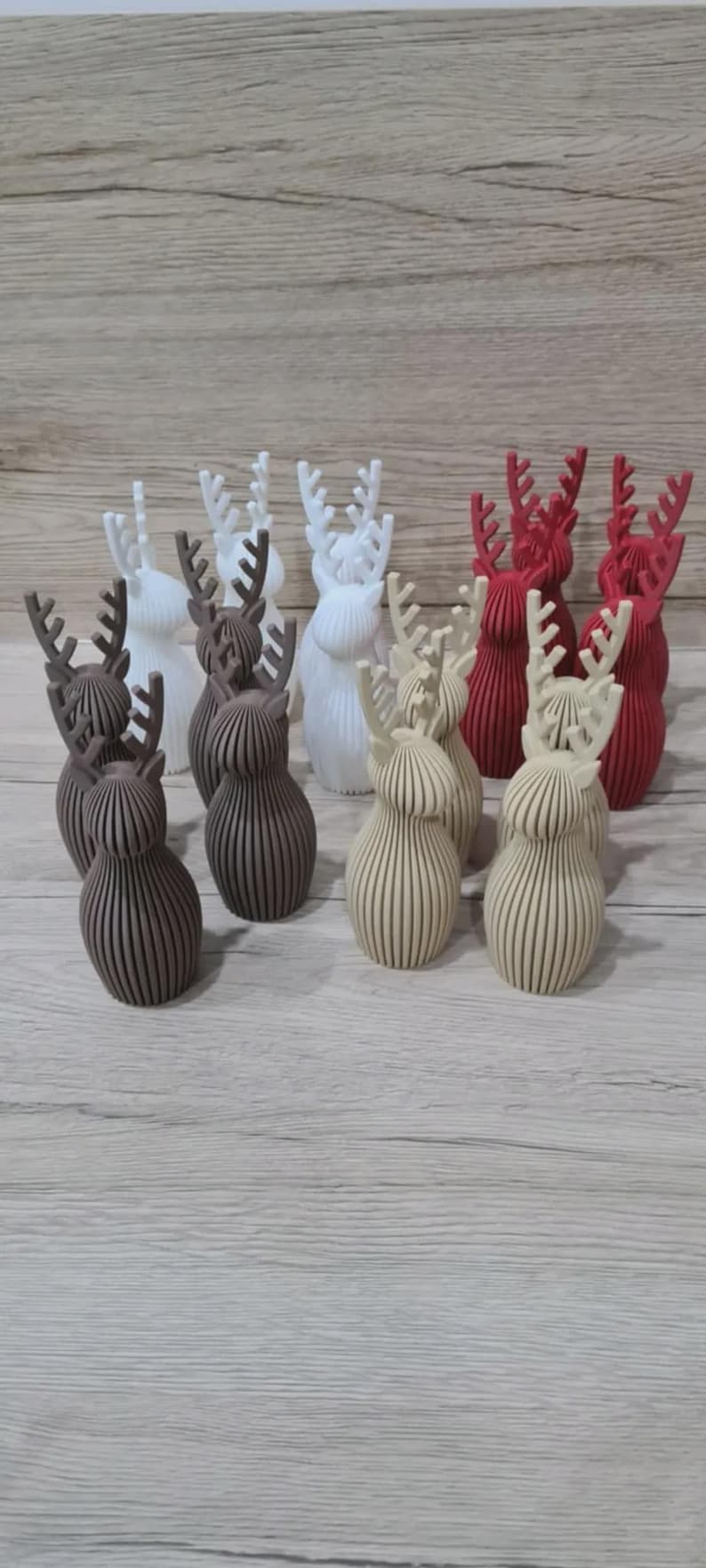 May include: A collection of twelve small, three-dimensional reindeer figurines arranged in rows. The figures are crafted with a ribbed, vertical texture and feature prominent antlers. They are available in four distinct colors: white, dark brown, beige, and red.