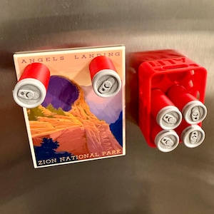 May include: A refrigerator magnet set featuring a Zion National Park image with two red soda can magnets. A red plastic carrier holds four additional soda can magnets. The cans have silver tops.