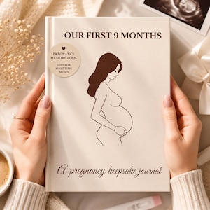 Puede incluir: Un diario de recuerdos de embarazo titulado "OUR FIRST 9 MONTHS". La portada presenta un dibujo lineal de una persona embarazada y el texto "PREGNANCY MEMORY BOOK" y "GIFT FOR FIRST TIME MOMS". El diario está abierto y sostenido por una persona.