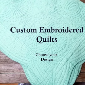 Puede incluir: Una manta acolchada de color verde claro con un diseño bordado personalizado. El texto en la manta dice "Custom Embroidered Quilts" y "Choose your Design".