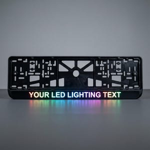 May include: Black license plate frame with the text "YOUR LED LIGHTING TEXT" illuminated in a rainbow of colors. The frame has a rectangular shape with various cutouts and a central mounting hole.