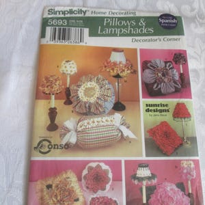May include: A Simplicity home decorating pattern for pillows and lampshades. The pattern features various designs, including floral-shaped pillows and lampshades with decorative trims. The cover includes the text "Decorator's Corner" and "sunrise designs by Jana Plus."