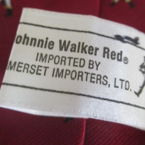 May include: Close-up of a white label with black text that reads "Johnnie Walker Red" and "Imported by Mersett Importers, Ltd." The label is on a red background, possibly fabric. A small silhouette of a person is on the right side of the label.