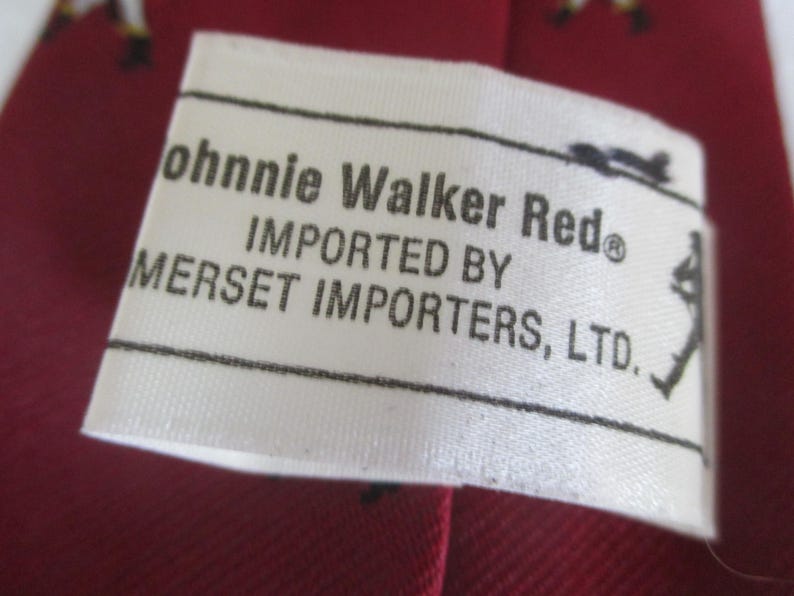 May include: Close-up of a white label with black text that reads "Johnnie Walker Red" and "Imported by Mersett Importers, Ltd." The label is on a red background, possibly fabric. A small silhouette of a person is on the right side of the label.