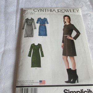 May include: A sewing pattern for a dress with three different styles. The pattern is by Cynthia Rowley and is for Simplicity pattern number 2084. The dress styles include a cowl neck, a short-sleeved dress with a belt, and a long-sleeved dress with cut-out sleeves.