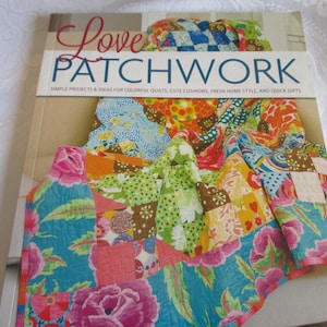 May include: A softcover book titled Love Patchwork with the subtitle Simple Projects & Ideas for Colorful Quilts, Cute Cushions, Fresh Home Style, and Quick Gifts. The cover features a vibrant, multi-colored patchwork quilt with floral patterns.