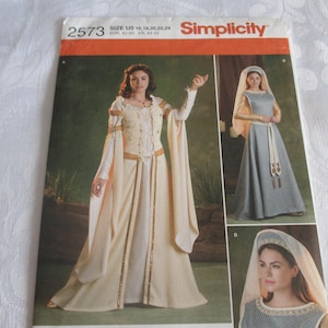 May include: Simplicity sewing pattern 2573 for a floor-length gown with long flowing sleeves and a matching headpiece. The pattern envelope displays two variations of the dress in cream and grey, featuring detailed trim and a medieval-inspired design.
