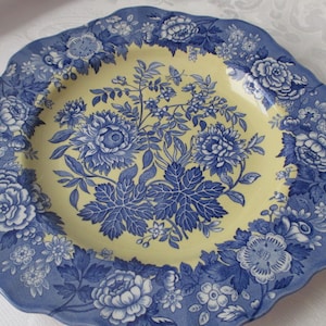 May include: A decorative ceramic plate with a scalloped edge. The plate features a blue floral design on a yellow background. The rim is blue with a repeating floral pattern. The plate is likely for decorative use.