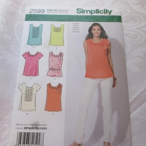 May include: A Simplicity sewing pattern featuring various blouse designs with ruffle details. The pattern includes a photo of a woman wearing an orange top and white pants. The pattern number is 2599.