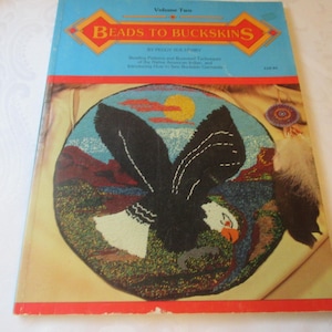 May include: A vintage book titled "Beads to Buckskins" with a cover illustration of an eagle in flight over a landscape. The book has a blue cover with red and orange accents. The eagle is black and white, and the background features a sun and mountains.