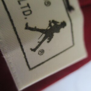 May include: Close-up of a white fabric tag with black text and a silhouette of a person holding a cane. The tag is on a red background. The text includes "RS, LTD."