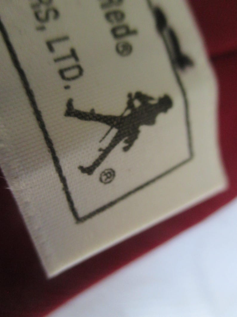 May include: Close-up of a white fabric tag with black text and a silhouette of a person holding a cane. The tag is on a red background. The text includes "RS, LTD."