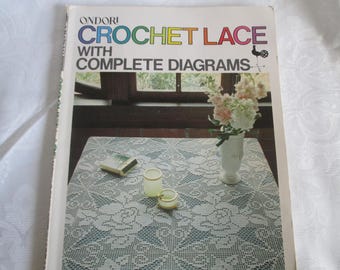 May include: A book titled "Ondori Crochet Lace with Complete Diagrams" featuring a white crocheted tablecloth with a floral design. The book cover also shows a vase with white flowers.