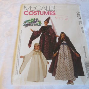 May include: A McCall's Costumes sewing pattern envelope 8937 for sizes 10 and 12. The front features illustrations of three outfits: a dark patterned gown with a pointed hat, a white dress with gold trim, and a hooded cloak over a floral dress.