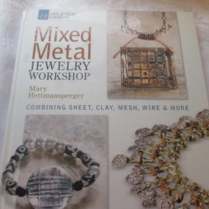 May include: A book titled "Mixed Metal Jewelry Workshop" by Mary Hettmansperger. The cover features jewelry examples, including a square pendant, a beaded bracelet, and a necklace. The book's subtitle is "Combining Sheet, Clay, Mesh, Wire & More."