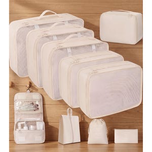 May include: A collection of off-white travel organizers and packing cubes. The set includes various sizes of zippered mesh cubes, a hanging toiletry bag, a shoe bag, a drawstring bag, and a small zippered pouch. All items have a clean, minimalist design.