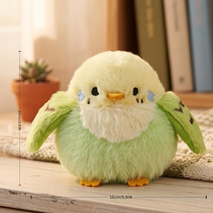 May include: A plush, round budgie bird toy, approximately 10cm/3.9in tall and 15cm/5.9in wide. The bird features a soft, light green body, yellow head, and small wings. It has black eyes, a yellow beak, and small blue accents.