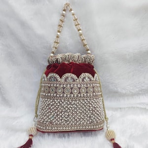 May include: An ornate, burgundy velvet pouch bag with intricate beadwork and a pearl-beaded handle. The bag features a detailed pattern of small white beads and gold embroidery, with matching tassels. The bag's interior is a deep burgundy color.