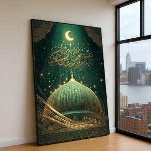 May include: A framed art print featuring a mosque dome in shades of green and gold. The artwork includes Arabic calligraphy, a crescent moon, and a starry night sky. The print is leaning against a white wall next to a window with a city view.
