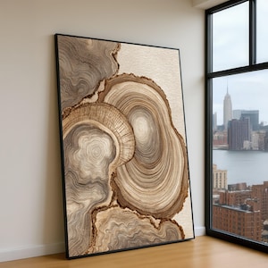May include: Large framed artwork featuring a detailed, abstract design resembling cross-sections of wood. The artwork showcases concentric circles and organic shapes in shades of brown and beige, creating a natural, textured appearance. The frame is black.